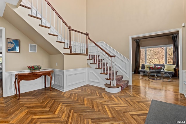 stairway featuring visible vents, wainscoting, and a high ceiling