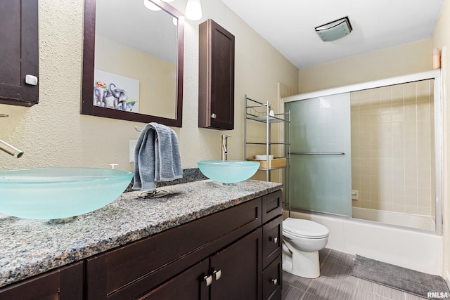 bathroom featuring double vanity, toilet, enclosed tub / shower combo, and a sink