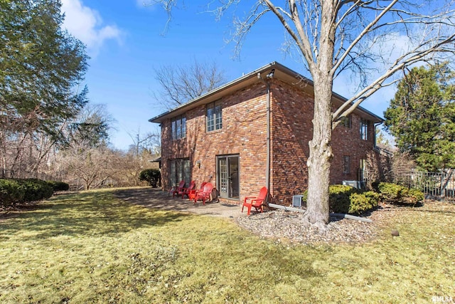 view of side of home featuring fence, brick siding, a lawn, and a patio area