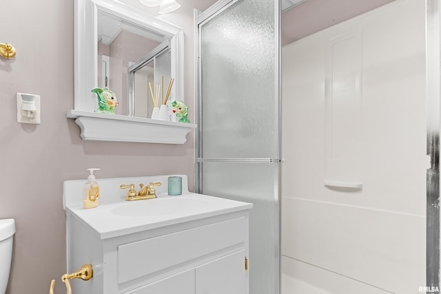 bathroom featuring toilet, vanity, and a shower with shower door