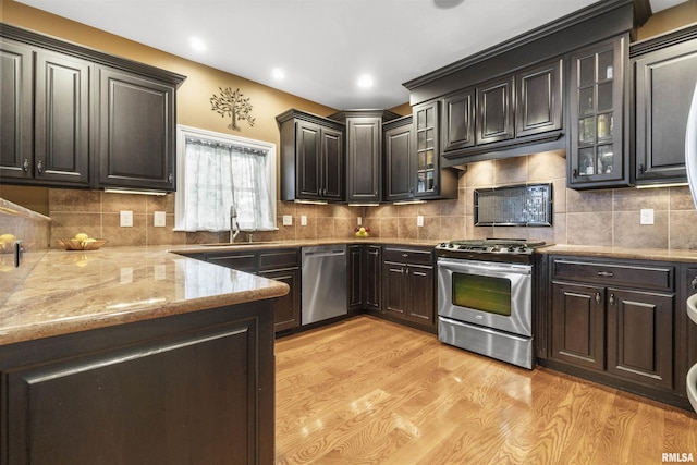 kitchen with decorative backsplash, appliances with stainless steel finishes, light wood-style floors, a sink, and light stone countertops