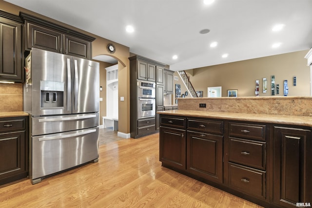 kitchen with dark brown cabinetry, arched walkways, appliances with stainless steel finishes, light countertops, and light wood-type flooring