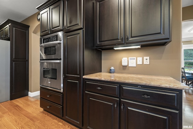 kitchen with light wood finished floors, stainless steel double oven, and light stone countertops