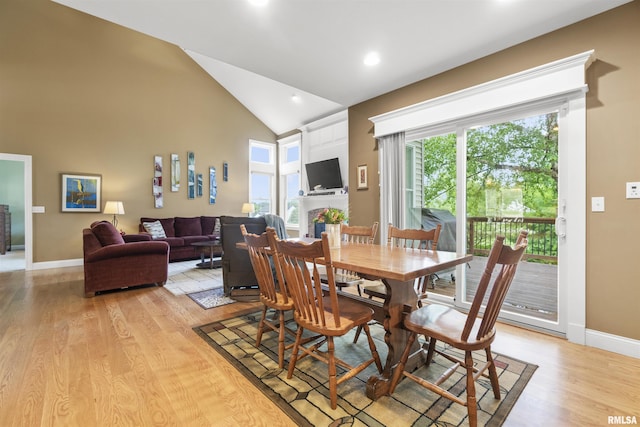 dining area with light wood-type flooring, a large fireplace, baseboards, and high vaulted ceiling