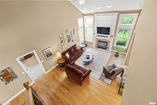 living room with a towering ceiling, a fireplace with flush hearth, ceiling fan, wood finished floors, and baseboards