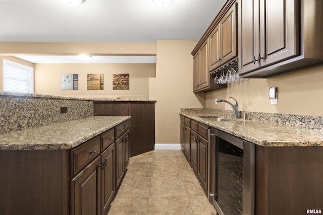 kitchen featuring wine cooler, a sink, dark brown cabinetry, and baseboards