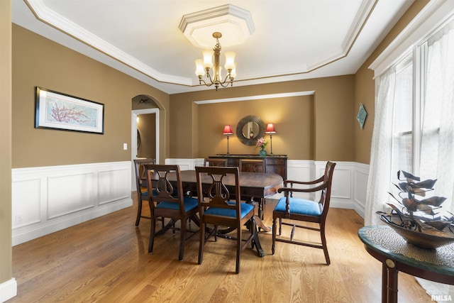 dining room with arched walkways, a notable chandelier, light wood-style floors, wainscoting, and a raised ceiling