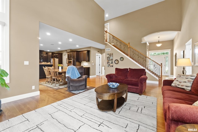 living room with high vaulted ceiling, a glass covered fireplace, light wood finished floors, and recessed lighting