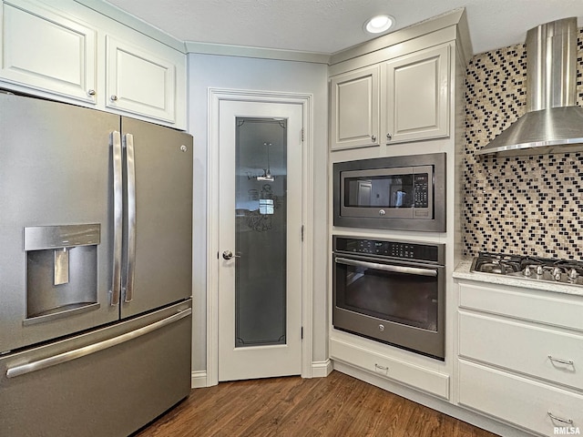 kitchen with dark wood-style floors, light countertops, appliances with stainless steel finishes, wall chimney exhaust hood, and backsplash