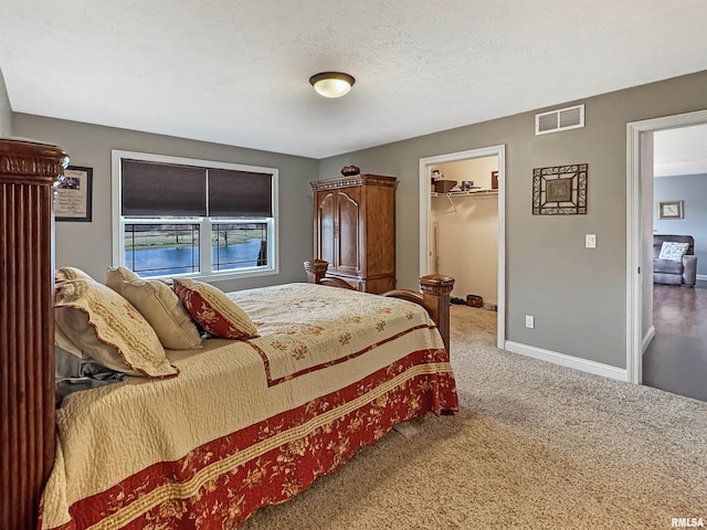 carpeted bedroom featuring visible vents, a textured ceiling, a closet, baseboards, and a spacious closet