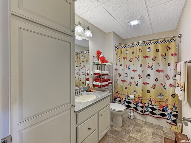 bathroom featuring shower / bath combo with shower curtain, toilet, stone finish floor, a drop ceiling, and vanity