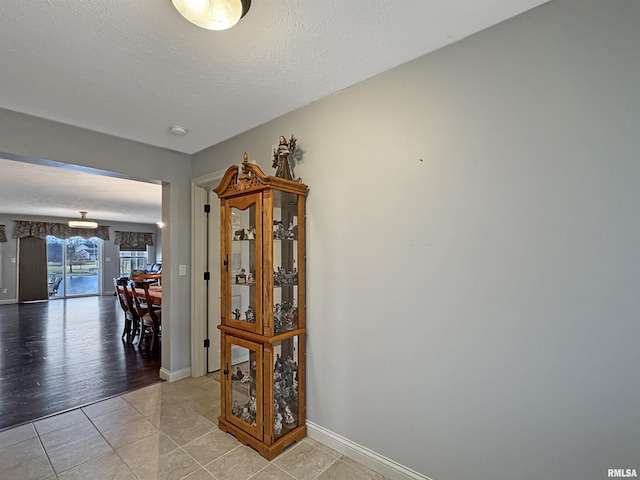 corridor featuring tile patterned flooring, baseboards, and a textured ceiling