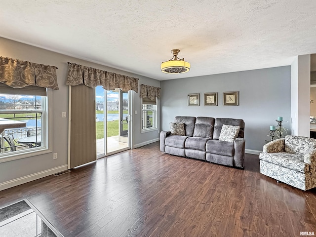 living room with visible vents, dark wood-style flooring, a wealth of natural light, and baseboards