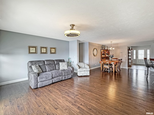 living area featuring a notable chandelier, a textured ceiling, baseboards, and wood finished floors