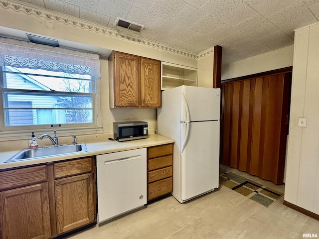 kitchen featuring light floors, visible vents, brown cabinetry, a sink, and white appliances