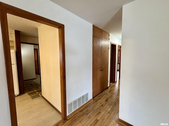 hallway with light wood finished floors, visible vents, and baseboards