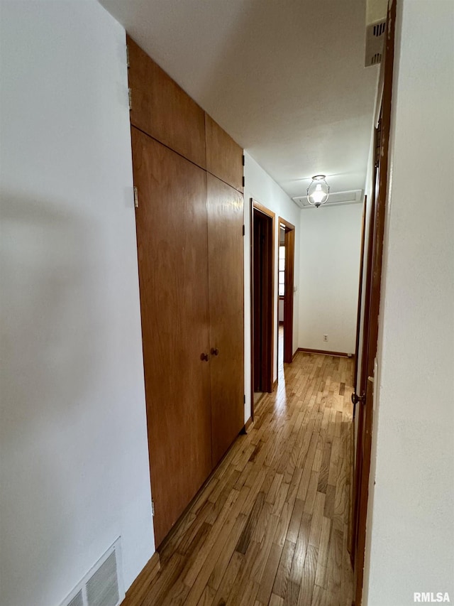 hallway with wood-type flooring, visible vents, and baseboards