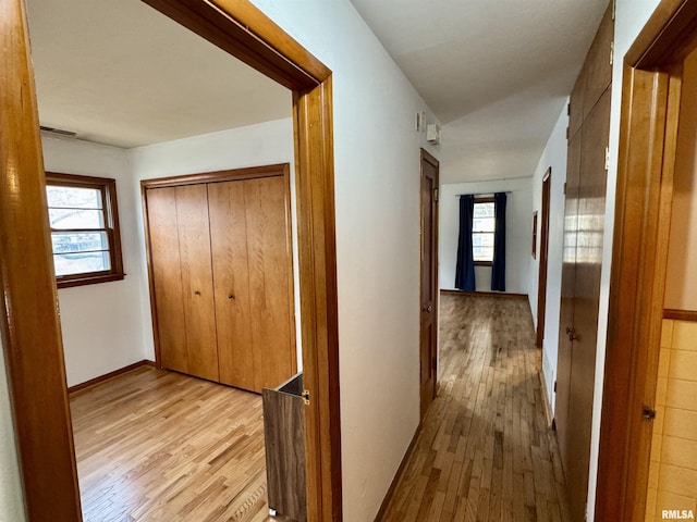 hallway with baseboards, visible vents, and light wood finished floors