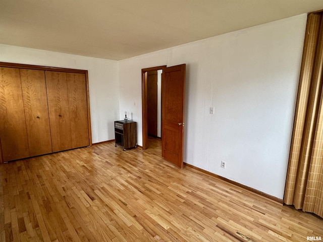 unfurnished bedroom featuring light wood-style flooring, baseboards, and a closet