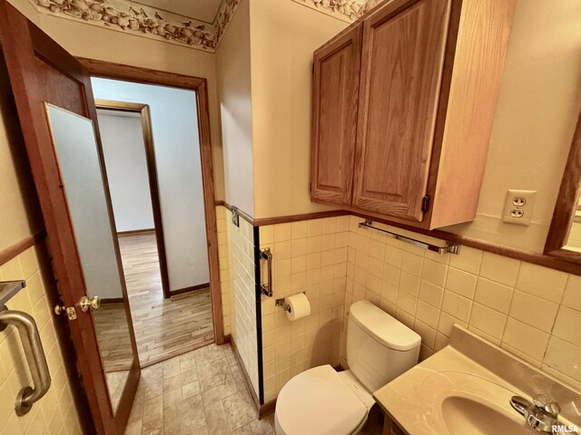 half bath with wainscoting, tile walls, toilet, and vanity