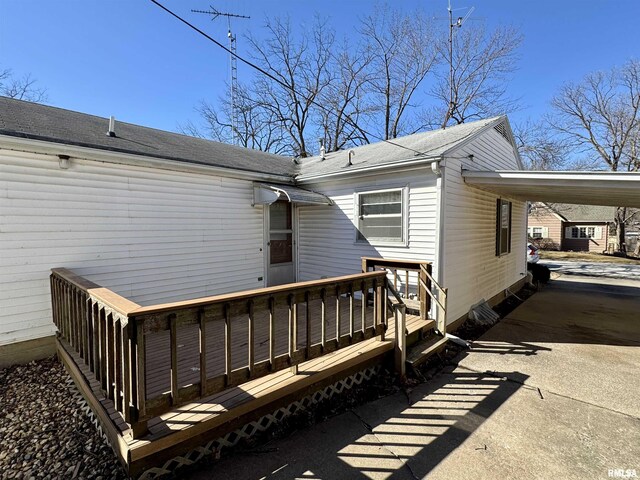 back of property featuring an attached carport, concrete driveway, roof with shingles, and a deck