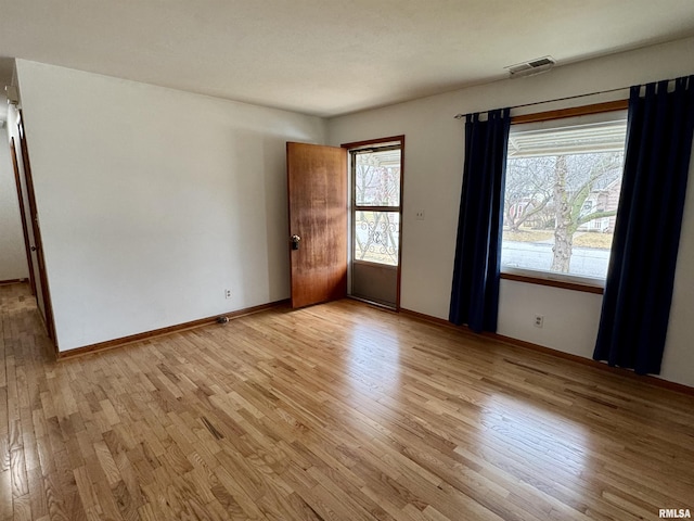 empty room with light wood-type flooring, visible vents, and baseboards