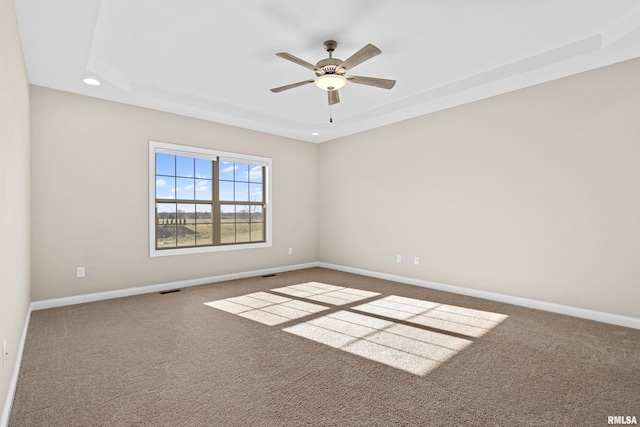 carpeted empty room with a ceiling fan, a tray ceiling, visible vents, and baseboards