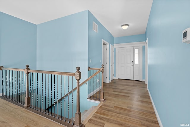 corridor with an upstairs landing, visible vents, baseboards, and wood finished floors