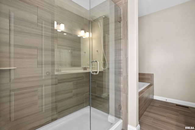 bathroom featuring a shower stall, a tub, and baseboards