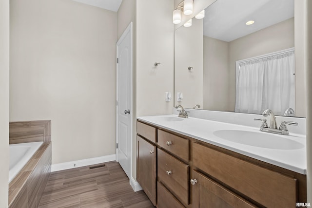 full bath with double vanity, tiled bath, baseboards, and a sink