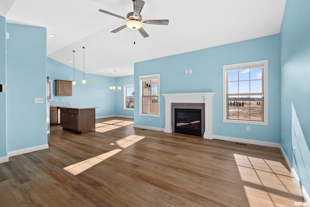 unfurnished living room featuring a healthy amount of sunlight, ceiling fan with notable chandelier, wood finished floors, and a glass covered fireplace