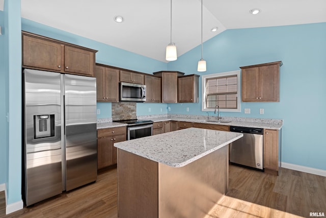 kitchen with appliances with stainless steel finishes, vaulted ceiling, a kitchen island, a sink, and wood finished floors