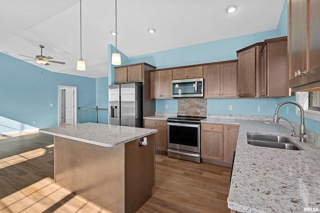 kitchen with a center island, decorative light fixtures, appliances with stainless steel finishes, a sink, and wood finished floors