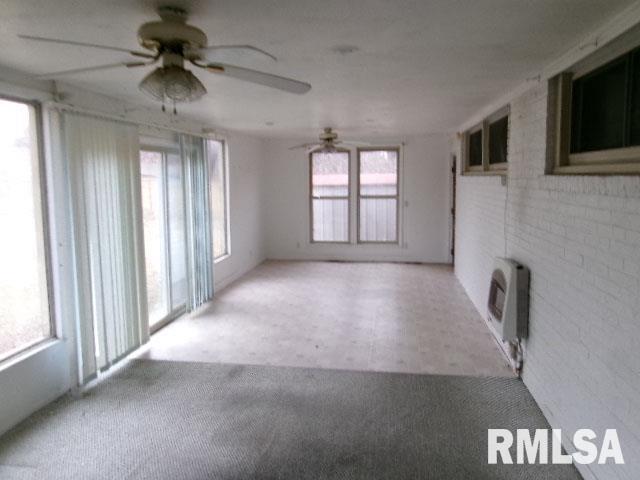 unfurnished room featuring a ceiling fan, brick wall, carpet flooring, and heating unit