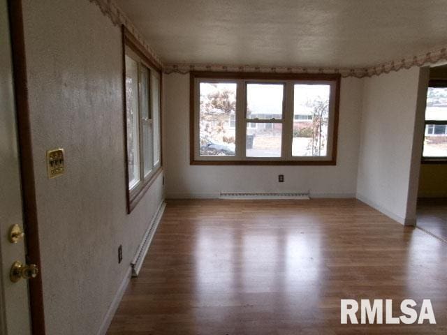 empty room with a baseboard radiator, wood finished floors, and a wealth of natural light