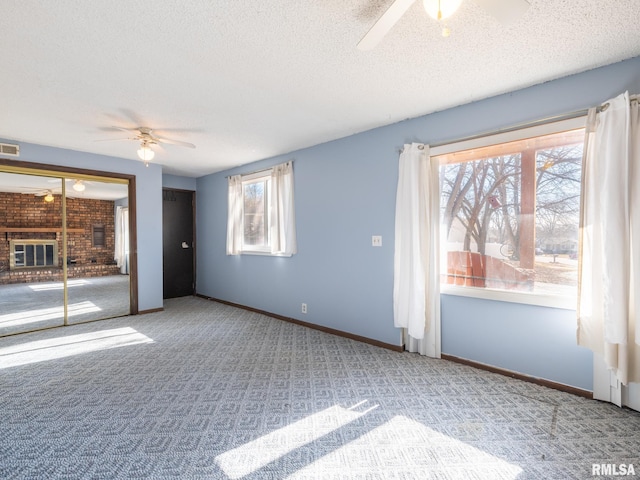 carpeted empty room with ceiling fan, a textured ceiling, a fireplace, visible vents, and baseboards