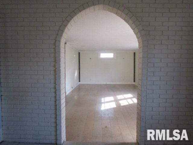 spare room with arched walkways, brick wall, and wood finished floors