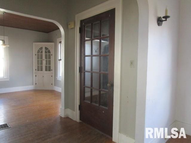 hall featuring arched walkways, wood finished floors, visible vents, and baseboards