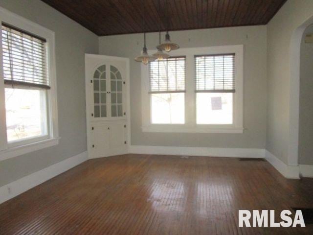 unfurnished dining area featuring wooden ceiling, baseboards, arched walkways, and hardwood / wood-style floors