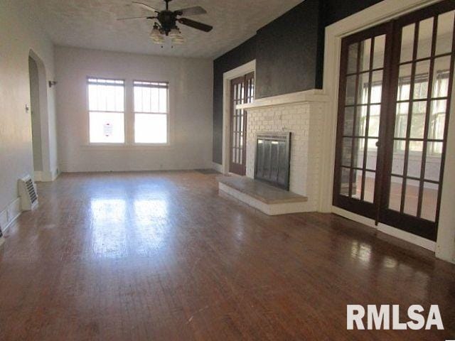 unfurnished living room featuring arched walkways, a fireplace, visible vents, ceiling fan, and wood finished floors