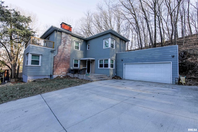 view of front of house with a chimney, driveway, a balcony, and an attached garage