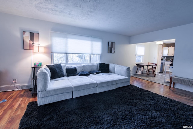 living area with visible vents, a healthy amount of sunlight, a textured ceiling, and wood finished floors