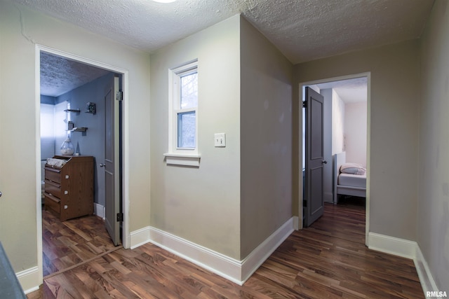 hallway featuring a textured ceiling, baseboards, and dark wood-type flooring