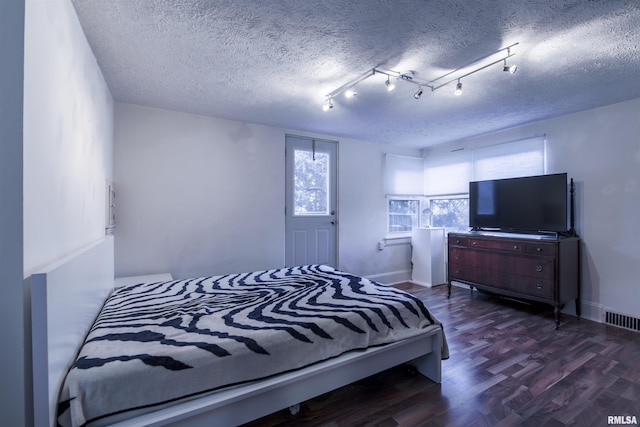 bedroom featuring baseboards, a textured ceiling, visible vents, and wood finished floors