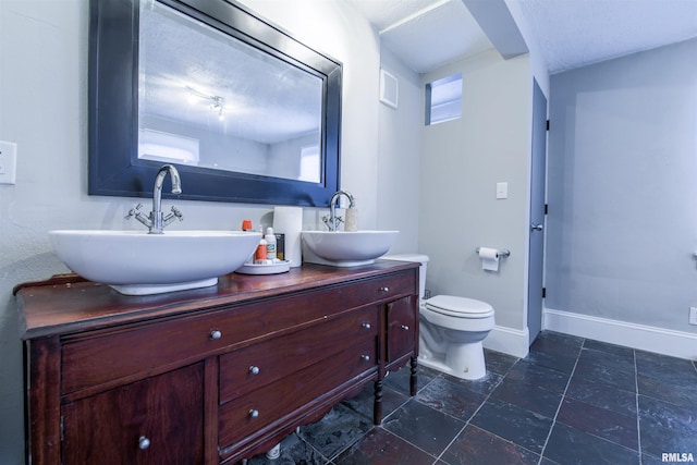 bathroom featuring toilet, a sink, baseboards, and double vanity