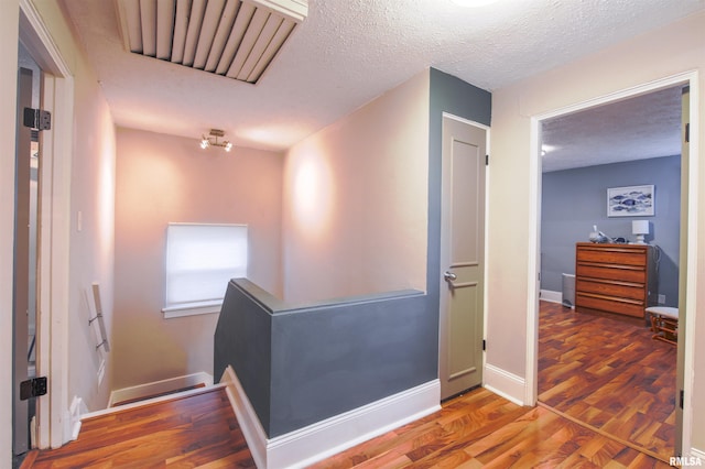 corridor featuring a textured ceiling, baseboards, wood finished floors, and an upstairs landing