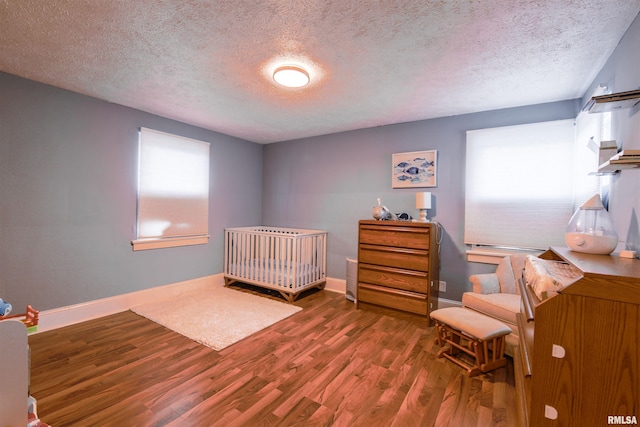 bedroom featuring a crib, a textured ceiling, baseboards, and wood finished floors