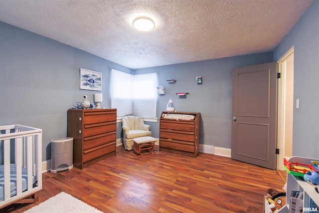 bedroom featuring a crib, a textured ceiling, baseboards, and wood finished floors