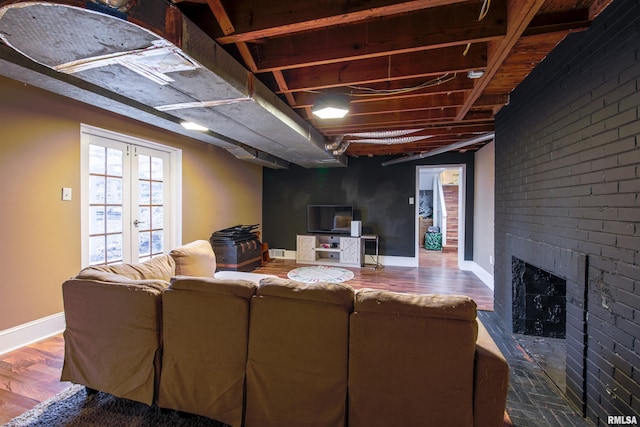 living area featuring a brick fireplace, baseboards, wood finished floors, and french doors