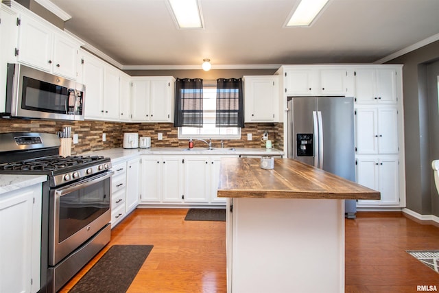 kitchen featuring light wood-style flooring, stainless steel appliances, white cabinetry, backsplash, and crown molding